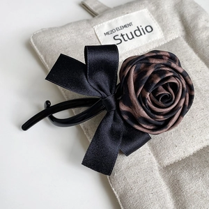 Detail of banana hair clip featuring leopard print fabric rose and black satin bow