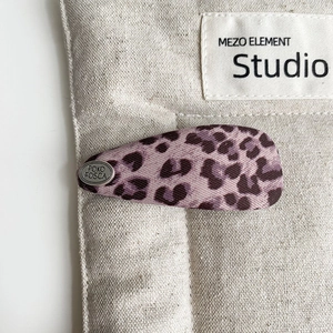 Close-up of purple leopard print hair clip with silver brand tag on a linen background