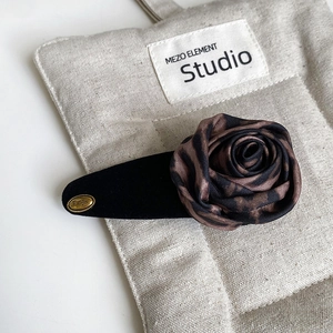 Macro detail of vintage leopard print silk rose hair clip with gold logo on beige linen