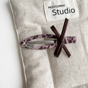 Close-up of handmade leopard fabric hair clip with leather bow and silver logo detail