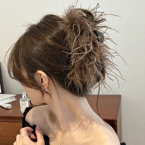 Detail view of a luxury brown ostrich feather hair claw clip worn on a model hair bun