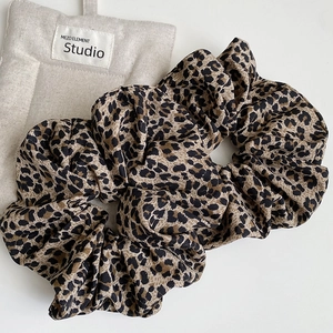 Close-up of leopard print scrunchie with soft fabric pleats on a minimalist beige background