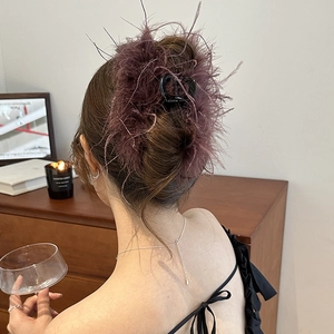 Detail of purple feather hair claw clip on model's hair with fluffy texture and elegant style