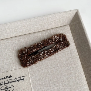 Close-up of brown knit BB hair clip on a beige fabric tray in a warm autumn aesthetic