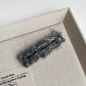 Close-up of rectangle tweed hair clip in grey bouclé fabric on display tray