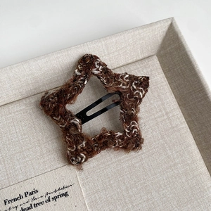 Close-up of a brown knit star hair clip with soft fuzzy texture and black metal BB base