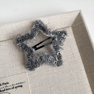 Detailed view of a star-shaped gray plush hair clip resting on a beige linen fabric tray