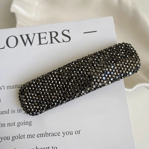 Macro shot of rectangular hair clip with dark grey rhinestones on a white card