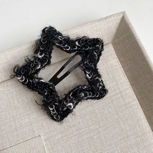 Detail of star-shaped black tweed hair clip with white plush yarn on beige linen tray