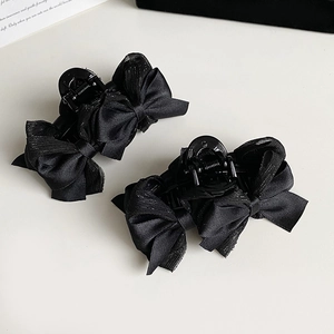 Détail de deux pinces à cheveux à nœud noir avec ruban pailleté et base brillante