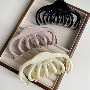 Three octopus hair claws in black, pink, and cream on a wooden jewelry display tray