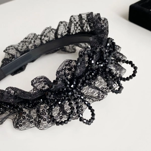 Gros plan d'un serre-tête en dentelle noire avec des perles brillantes et des volants