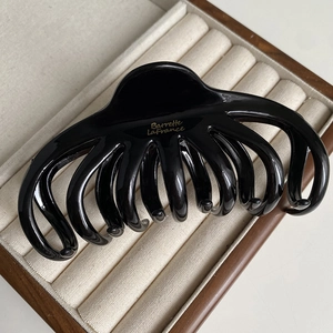 Detailed macro view of a glossy black octopus claw clip inside a beige jewelry gift box