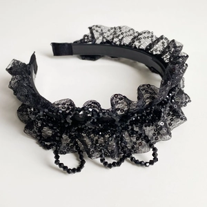 Détail d'un serre-tête en dentelle noire avec paillettes et chaînes de perles
