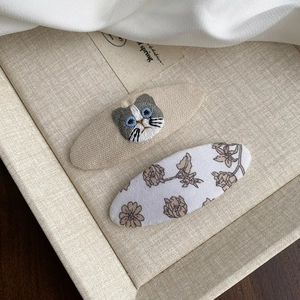 Détail de barrettes en tissu avec chat brodé et motif floral sous un éclairage doux