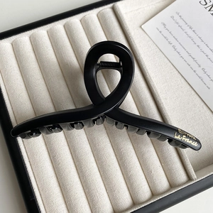 Close-up of matte black hair claw with gold lettering on a beige velvet tray