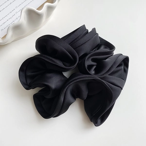 Détail d'un grand chouchou en satin noir avec des bords à volants élégants sur blanc
