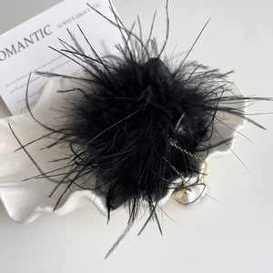 Détail d'une pince à cheveux en plumes noires avec pampilles dorées et perles sur plat