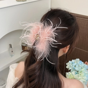 Elegant large pink feather hair claw clip on brunette hair in a soft indoor setting