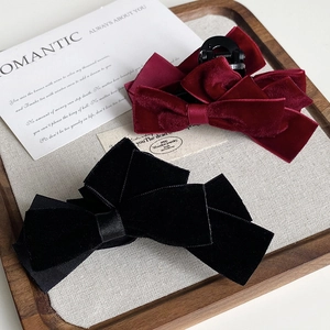 Detailed macro view of black and burgundy velvet bow hair claws on a wooden tray