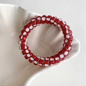 Élastique à cheveux spirale rouge à pois blancs dans une coupelle en céramique blanche