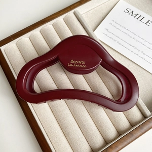 Close-up of a matte burgundy heart claw clip with golden lettering on a velvet tray