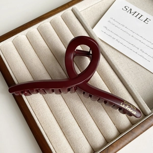 Detail of a large wine red resin hair claw with golden lettering on a jewelry tray