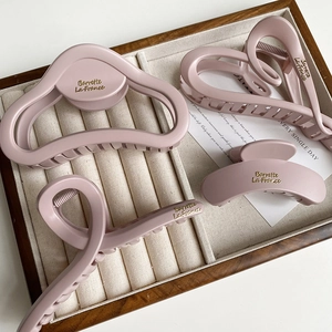 Elegant set of 4 matte pink hair claws with gold logo on a wooden display tray