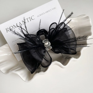 Elegant black bow hair claw clip with delicate feathers and rhinestones on shell tray