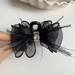 Elegant black mesh bow hair claw with dual crystals and feathered fringe on white tray