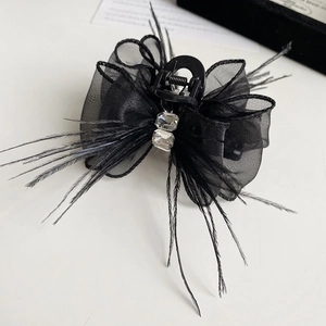 Detailed close-up of a black mesh bow hair claw with feathers and sparkling rhinestones