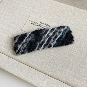 Detail of knit wool hair clip featuring grey and black woven texture with white stitching