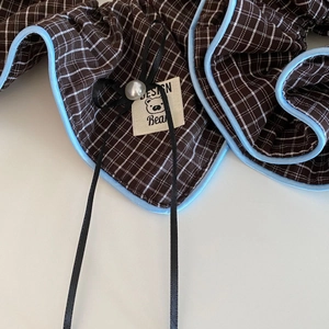 Detail eines karierten Haargummis mit schwarzer Schleife, Perle und Bären-Etikett