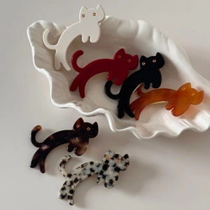Close-up of 6 colorful cat-shaped acetate hair clips in various patterns on a ceramic plate