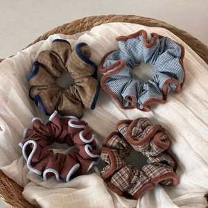Detailed view of four large plaid and striped fabric scrunchies with plush contrast edges