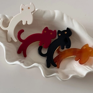 Detail view of acetate cat hair clips in four colors on a white shell-shaped tray