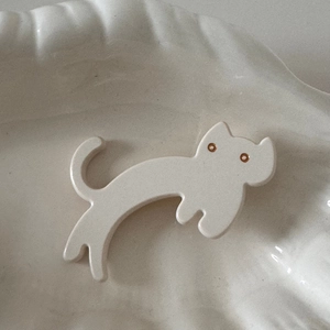 Close-up of cream-white acetate cat hair clip with glossy finish and gold eyes details