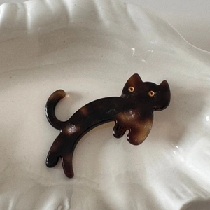 Macro detail of cute cat acetate hair clip with tortoiseshell texture on a white ceramic tray
