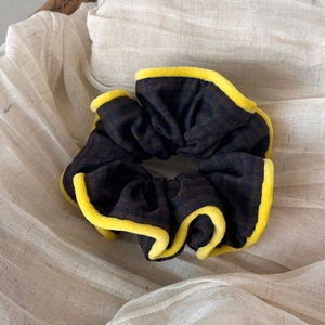 Detailed view of coffee plaid fabric scrunchie with yellow plush trim on rustic background