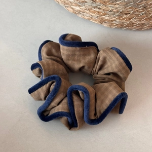 Detail of a brown fabric scrunchie with dark blue velvet trim and pleated texture