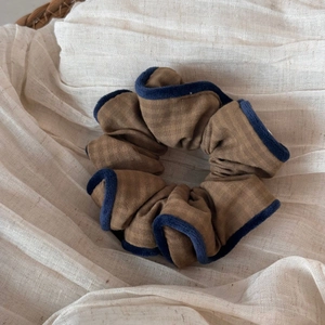 Detail of brown plaid scrunchie with navy blue edges on a textured fabric background