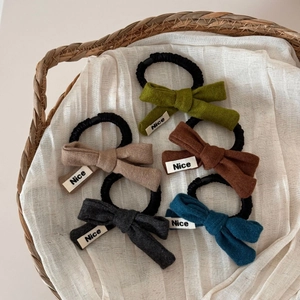 Détail de cinq chouchous en tricot avec étiquettes 'Nice' dans un panier en osier