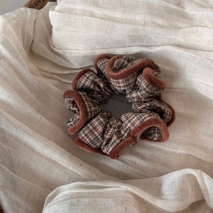 Macro shot of stylish plaid hair scrunchie with warm brown plush trim on woven basket