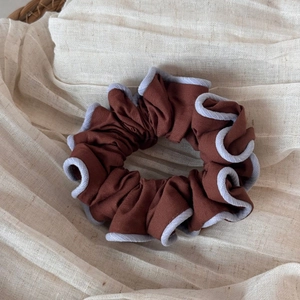 Detail of a dark brown fabric scrunchie with light blue piped edges on linen