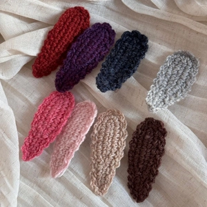 Close-up of hand-knitted wavy wool hairpins in eight colors on white fabric