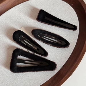 Detail of four geometric black suede hair clips with brown stitching on a textured base