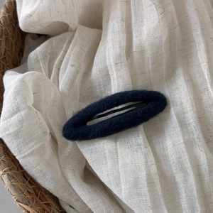 Close-up of navy blue wool texture oval BB hair clip on a soft white fabric