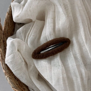 Detail of dark brown faux fur oval BB hair clip on textured white linen fabric