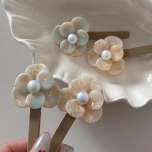 Elegant acetate flower hair clips with marble texture and pearl accents on shell dish