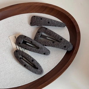 Close-up of four dark grey polka dot wool hair clips in a rustic wooden tray